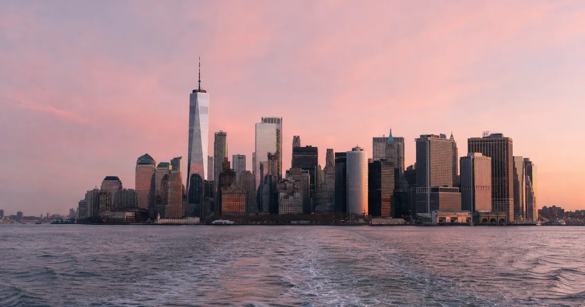 A downtown financial-district office tower at dusk with glass walls reflecting the city skyline, viewed from a quiet mezzanine