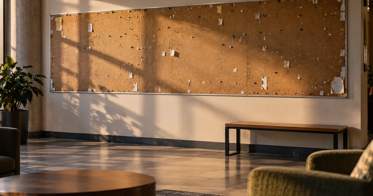 A long student-union bulletin wall stripped of job flyers down to bare pushpins and torn paper corners, late-afternoon light across an empty lounge