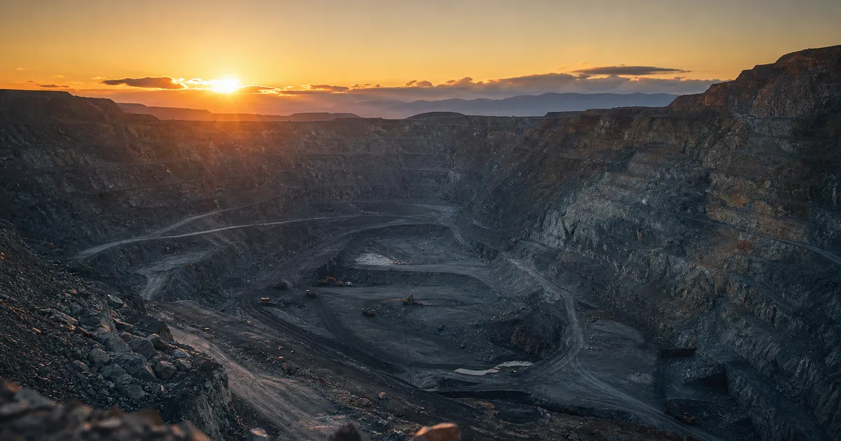 An open-pit mine at sunrise with terraced rock walls and heavy equipment small in the distance, dramatic geological scale, no people
