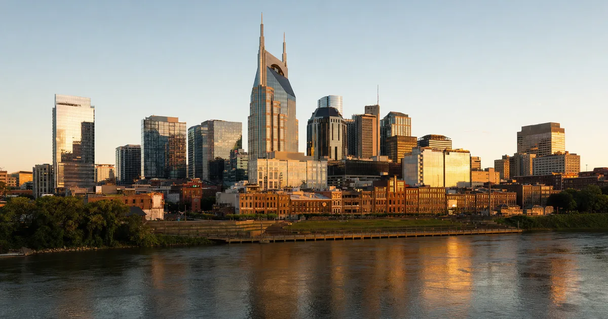 Downtown Nashville skyline at dusk reflected in the Cumberland River with modern office towers and a pedestrian bridge in the foreground