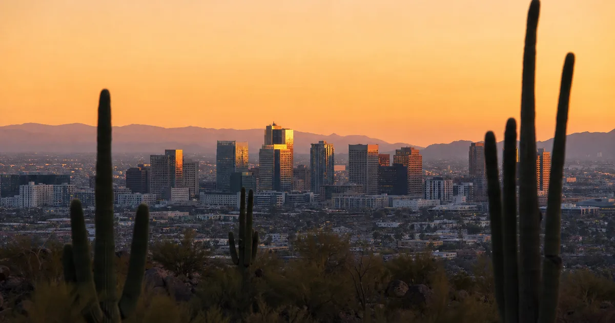 A wide-angle view of a modern semiconductor fabrication facility exterior in the Arizona desert at dusk, with mountain silhouettes and warm ambient lighting