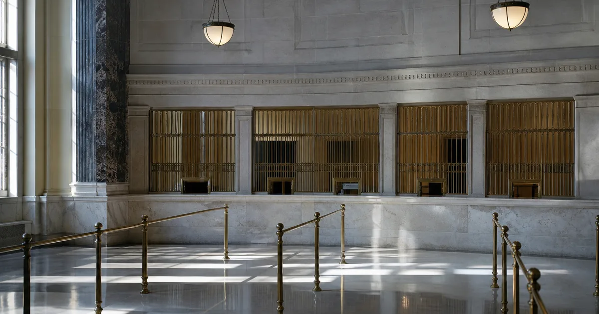 A university bursar hall at midday, a long marble counter and brass grille windows with an empty queue rail, cool daylight raking across polished stone