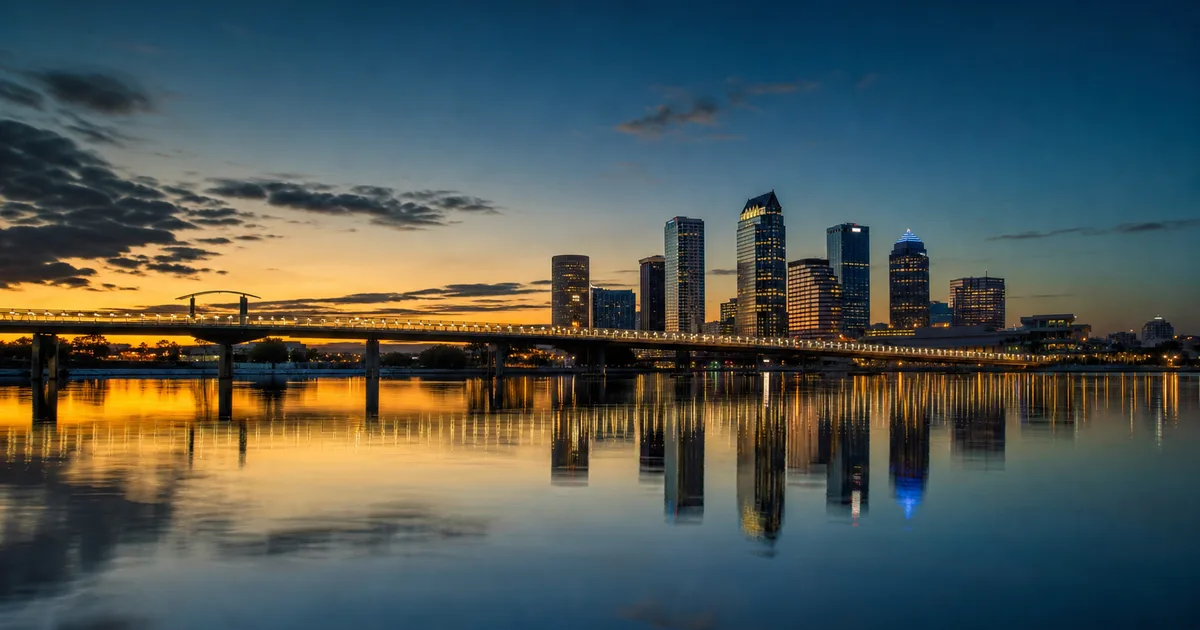 Downtown Tampa skyline reflected in the Hillsborough River at dusk with office towers lit in blue and gold against a clear sky