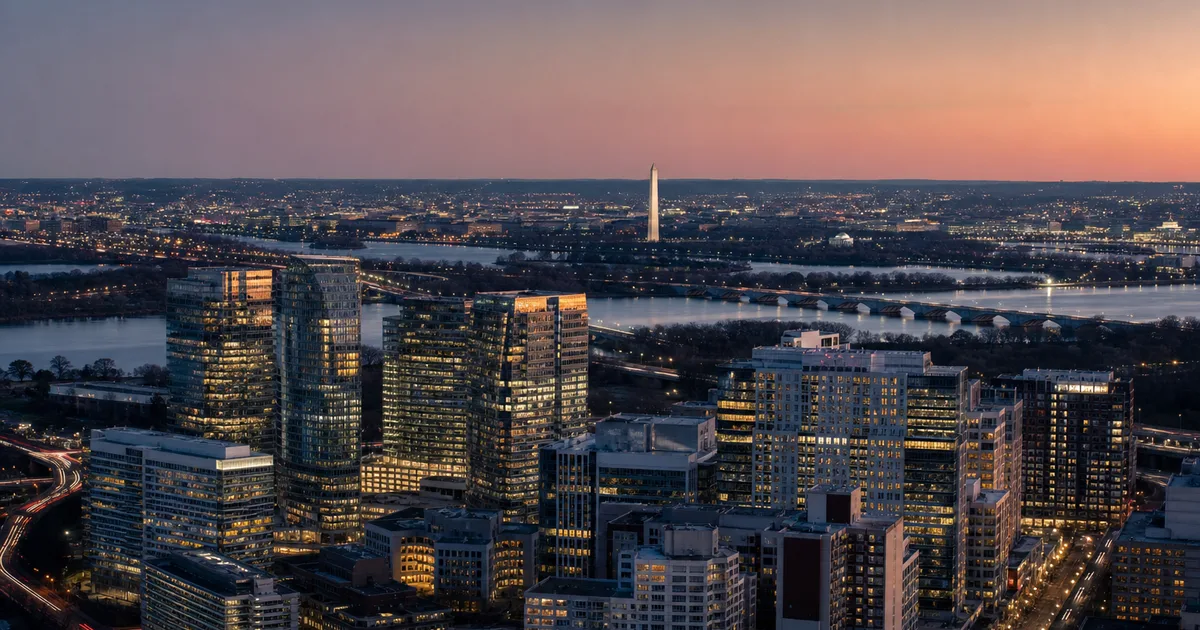Aerial view of the Rosslyn-Ballston tech corridor in Northern Virginia at dusk, a dense cluster of glass towers glowing across the Potomac from the