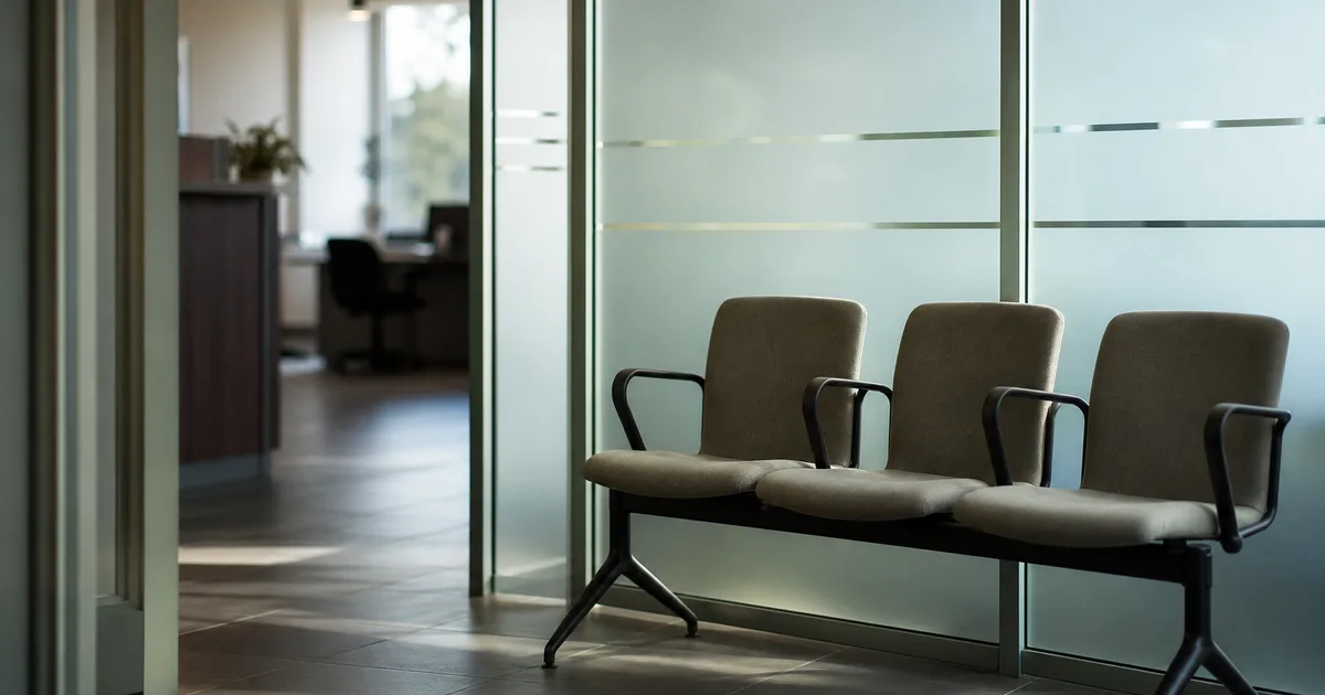 A downtown legal aid office reception at midday, empty waiting chairs beside a frosted glass partition